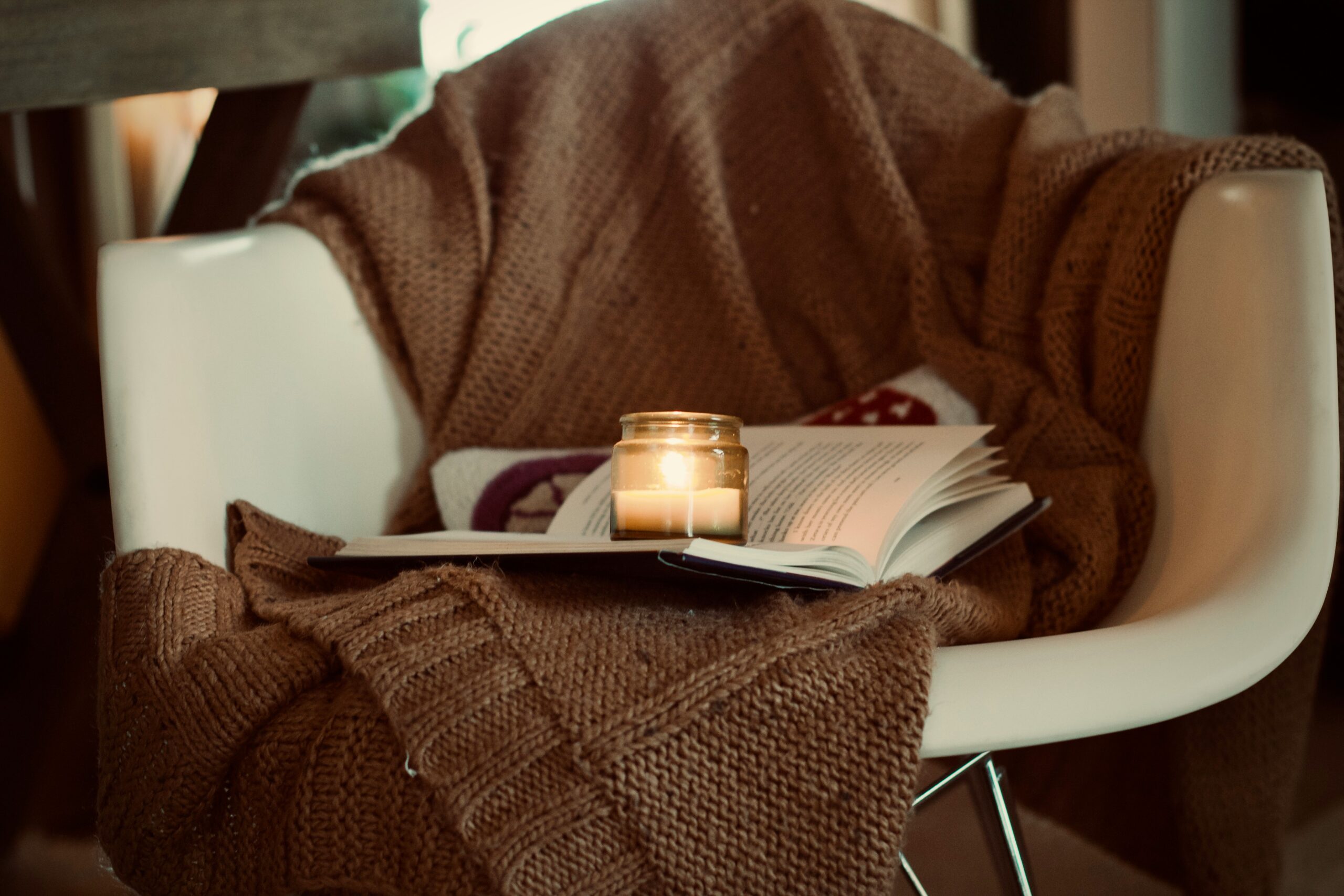 Gemütliche Leseecke für Herbst und Winter mit Buch, Strickdecke und warmem Licht